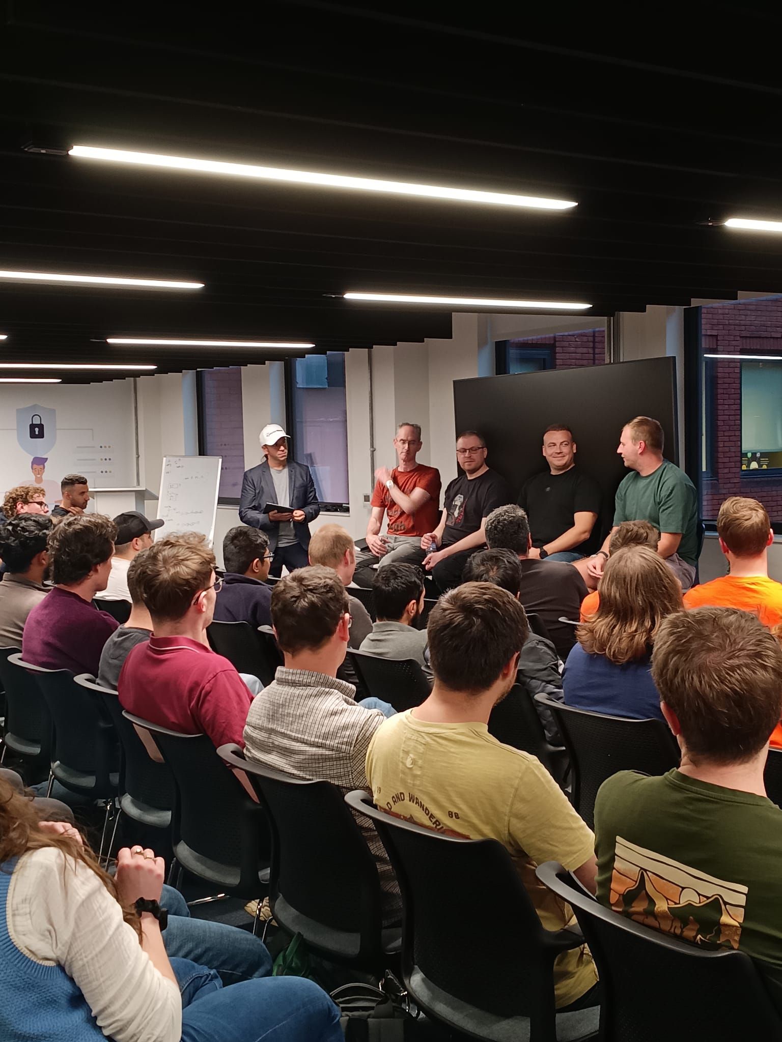 The four Ground Truth panellists seated at the front of the room, smiling, with the moderator standing beside them holding notes